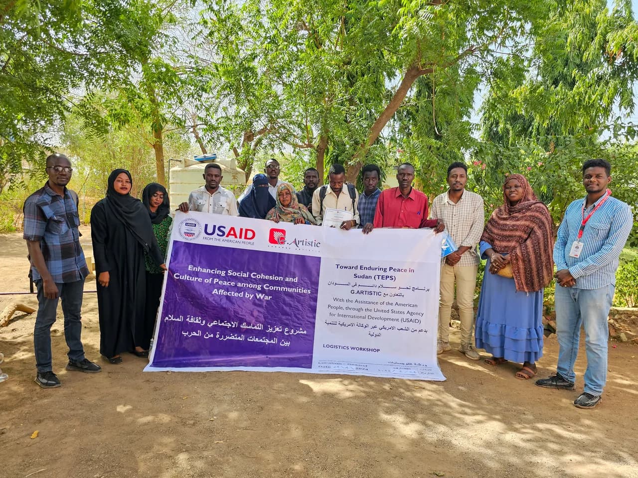 أعضاء من فريق جي ارتستك يحملون لافتة مشروعٍ مموَّل للتماسك الاجتماعي في السودان.