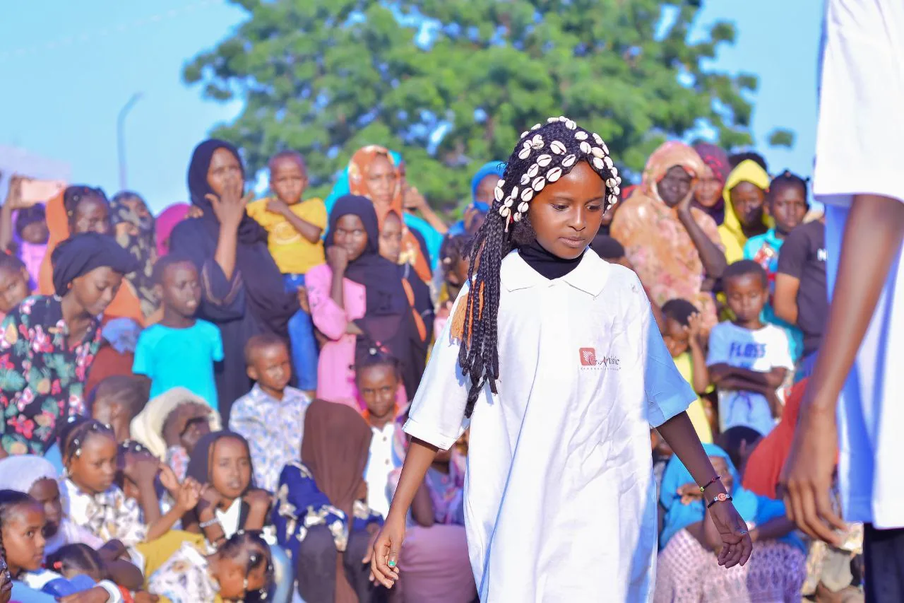 A young performer in a white shirt before a large seated audience at an outdoor community event.