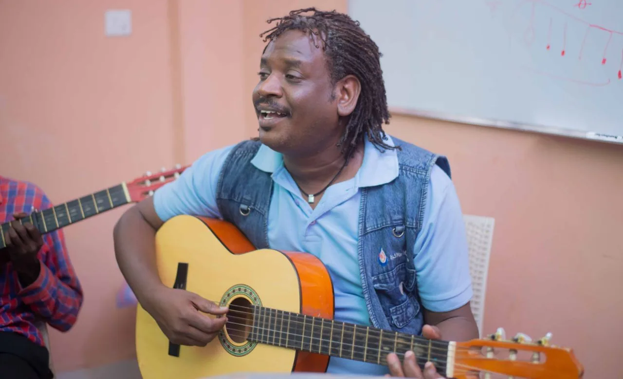 A young musician playing guitar in a workshop circle.