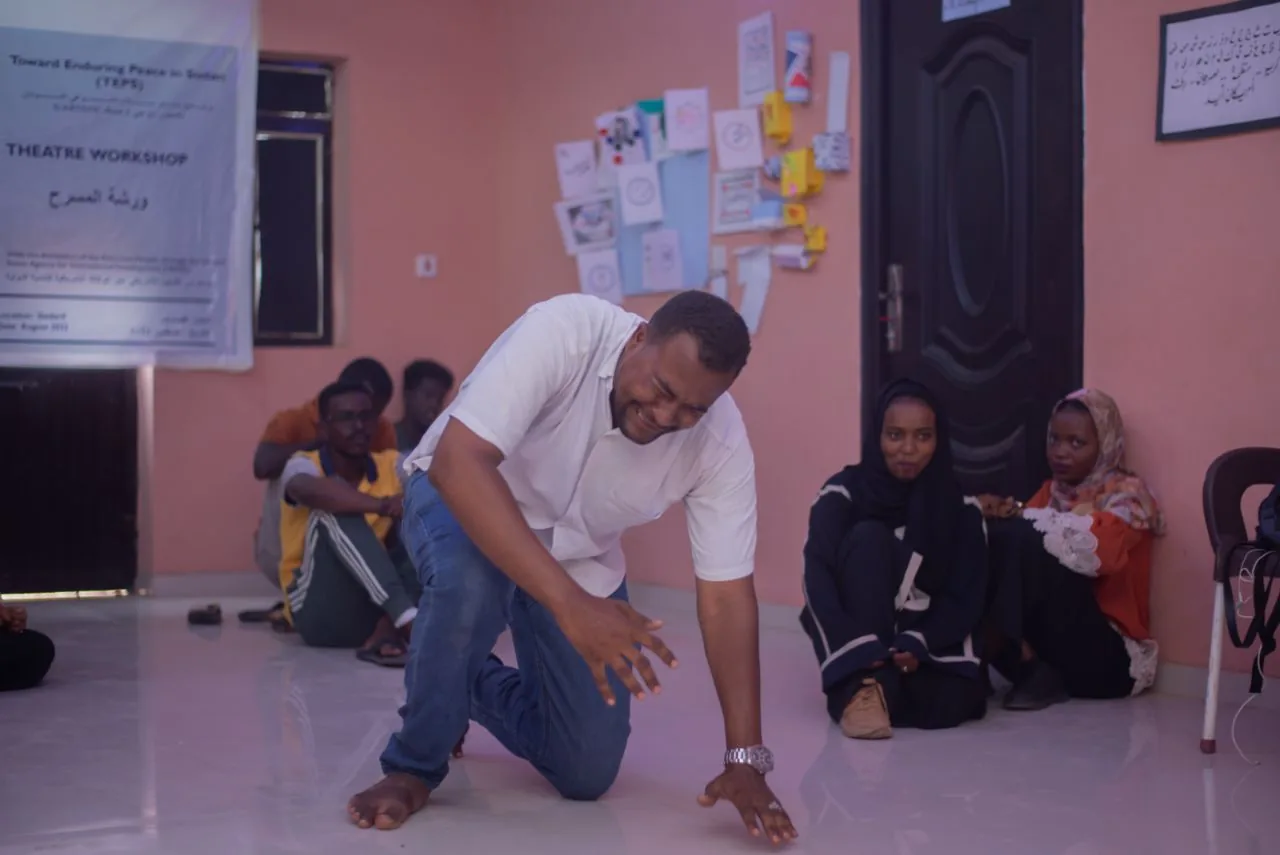 A facilitator acting out a scene on the floor during a theatre workshop, with participants seated and watching.